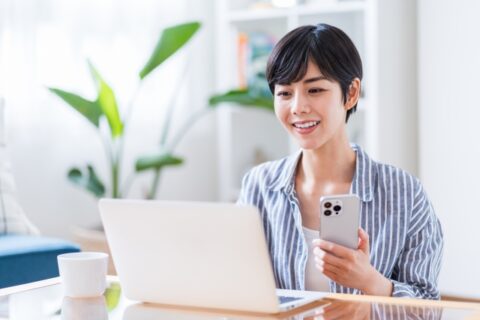 スマートフォンを手にしながらノートパソコンでページを確認する人物
