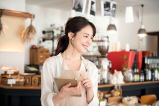 オンラインストア運営のため、タブレットを持つカフェ店員の女性